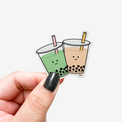 A cute sticker featuring a cup of matcha milk tea with boba and regular milk tea with boba with happy faces on them.