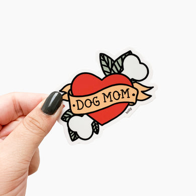 A funny sticker with a play on the popular mom tattoo with the heart and arrow through it, but has a dog bone and leaves instead with text that reads, Dog Mom.