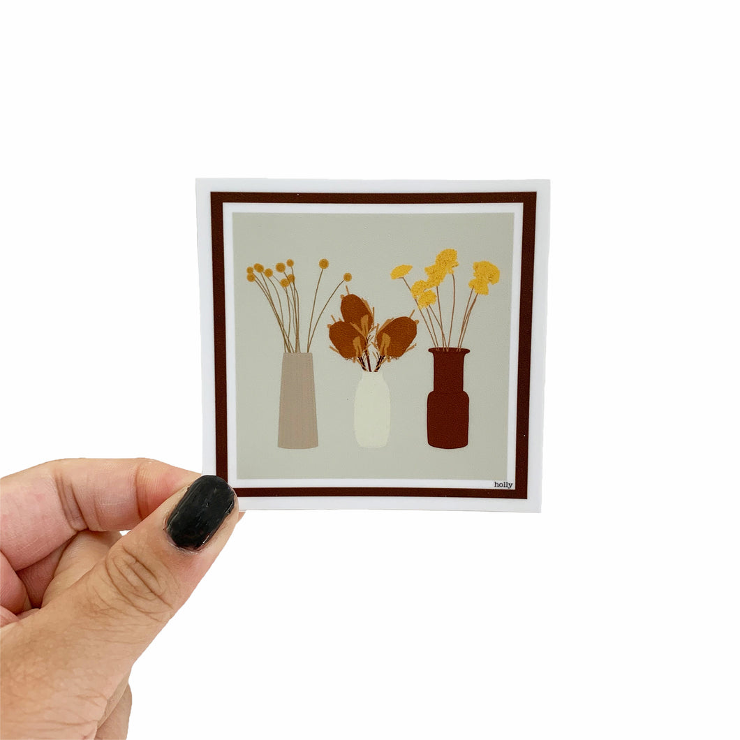 A sticker featuring different dried flowers in three unique warm-toned vases.