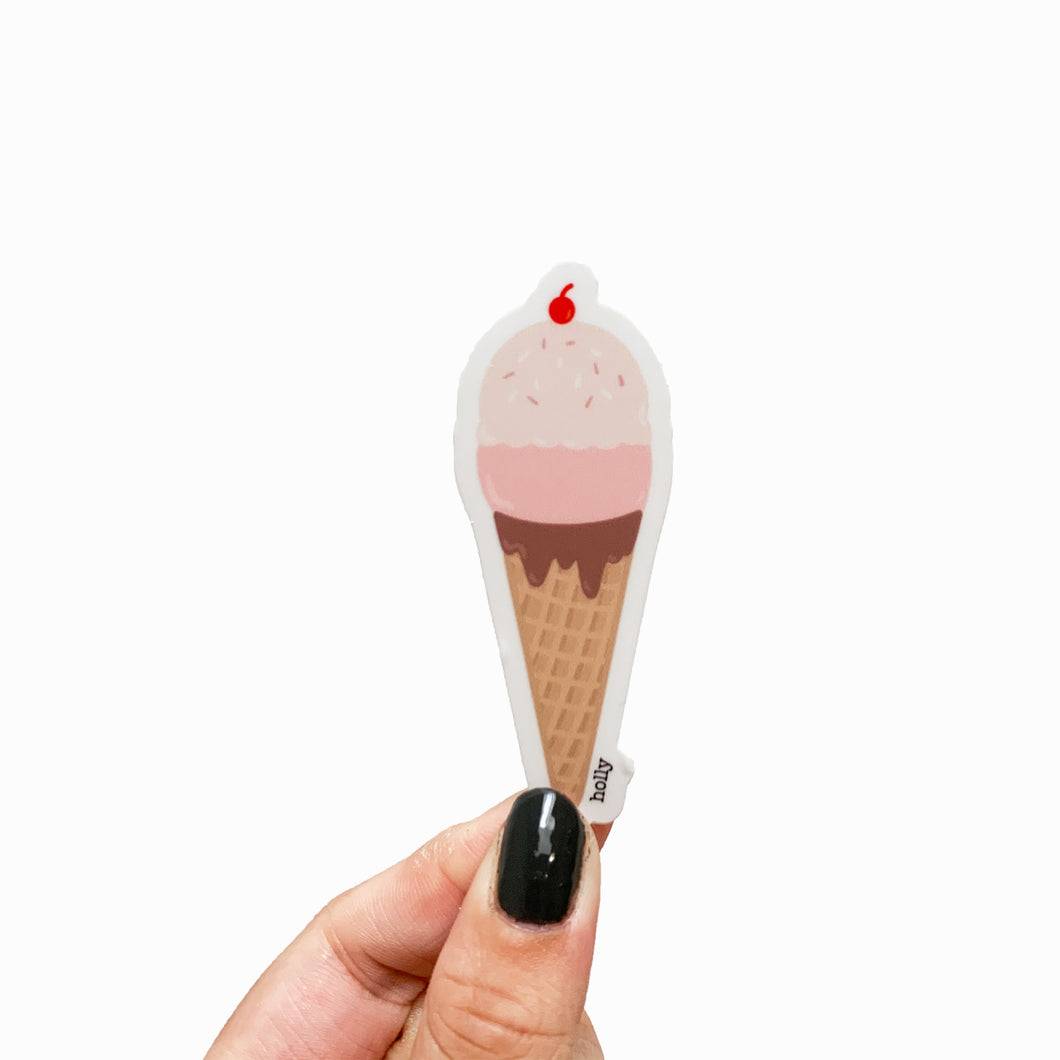 A sticker featuring strawberry ice cream with sprinkles and a cherry on top in a chocolate dipped waffle cone.